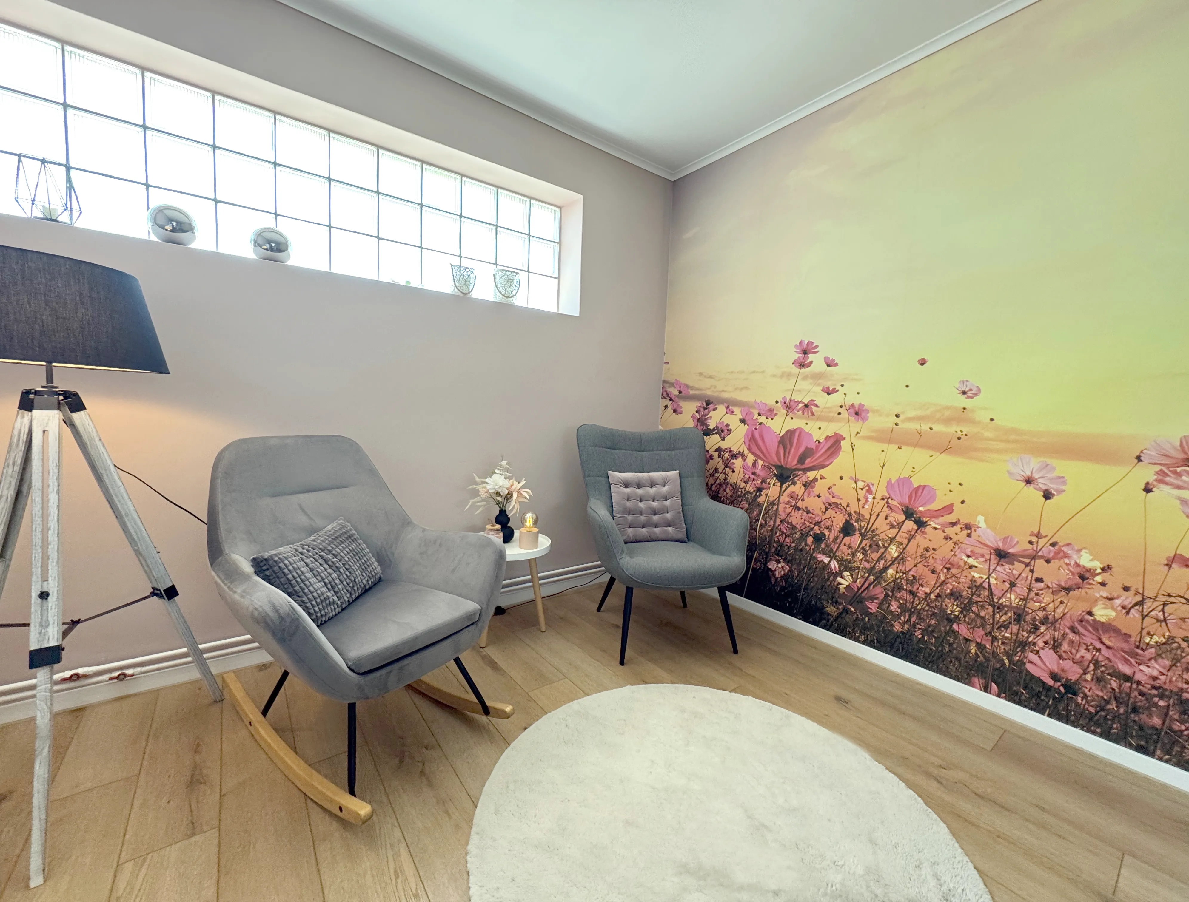 Warte- und Ruheraum mit zwei gemütlichen Stühlen in grauer Farbe. Die Wandtapete zeigt eine wunderschöne Blumenwiese mit einem Himmel in warmen gelb, orange Farbtönen